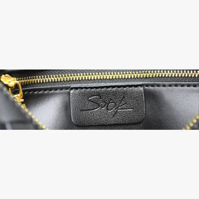 Gros plan de l’intérieur d’une pochette en cuir noir tressé avec zip doré et patch logo embossé