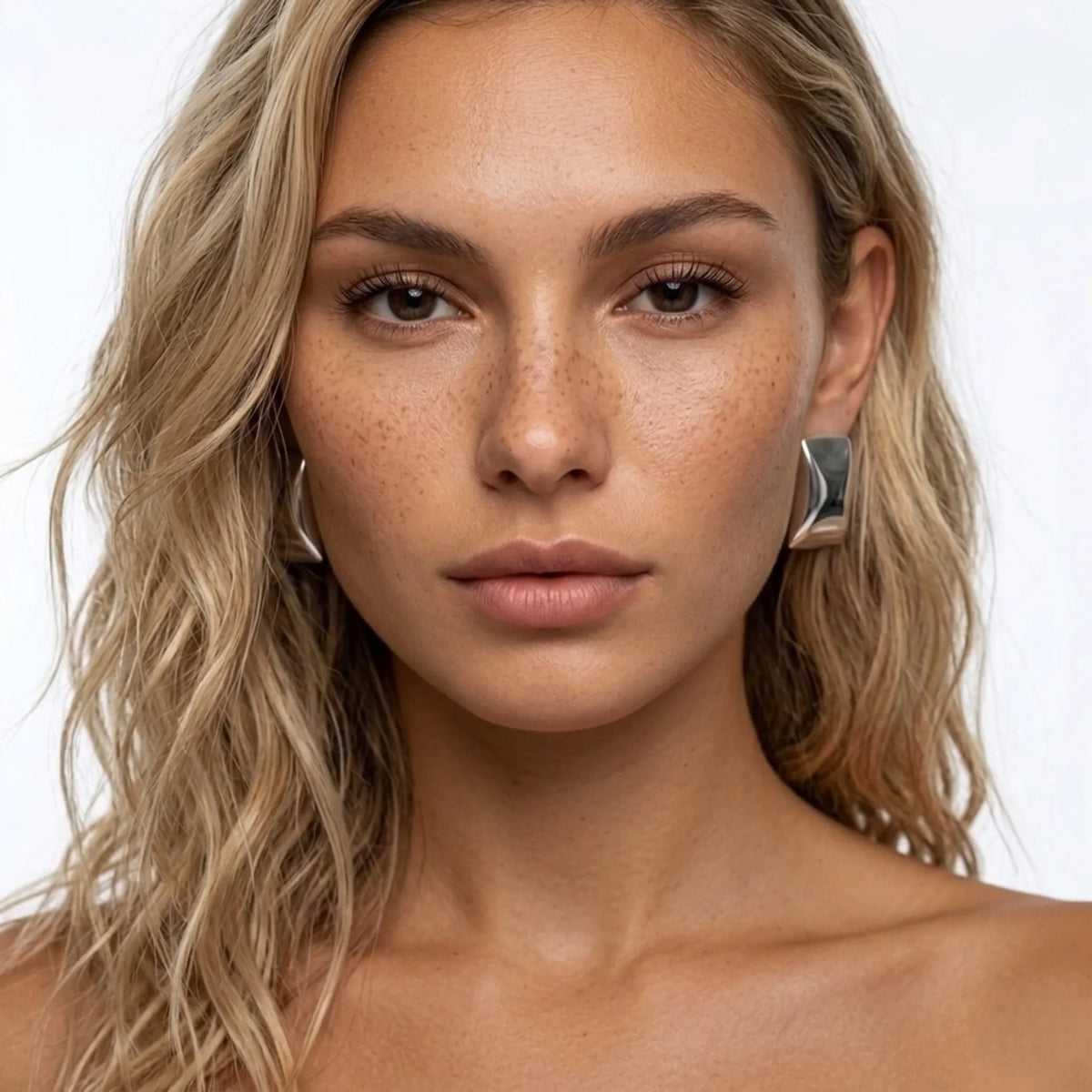 Nahaufnahme of a woman with blonde hair and freckles wearing silver earrings vor weissem Hintergrund