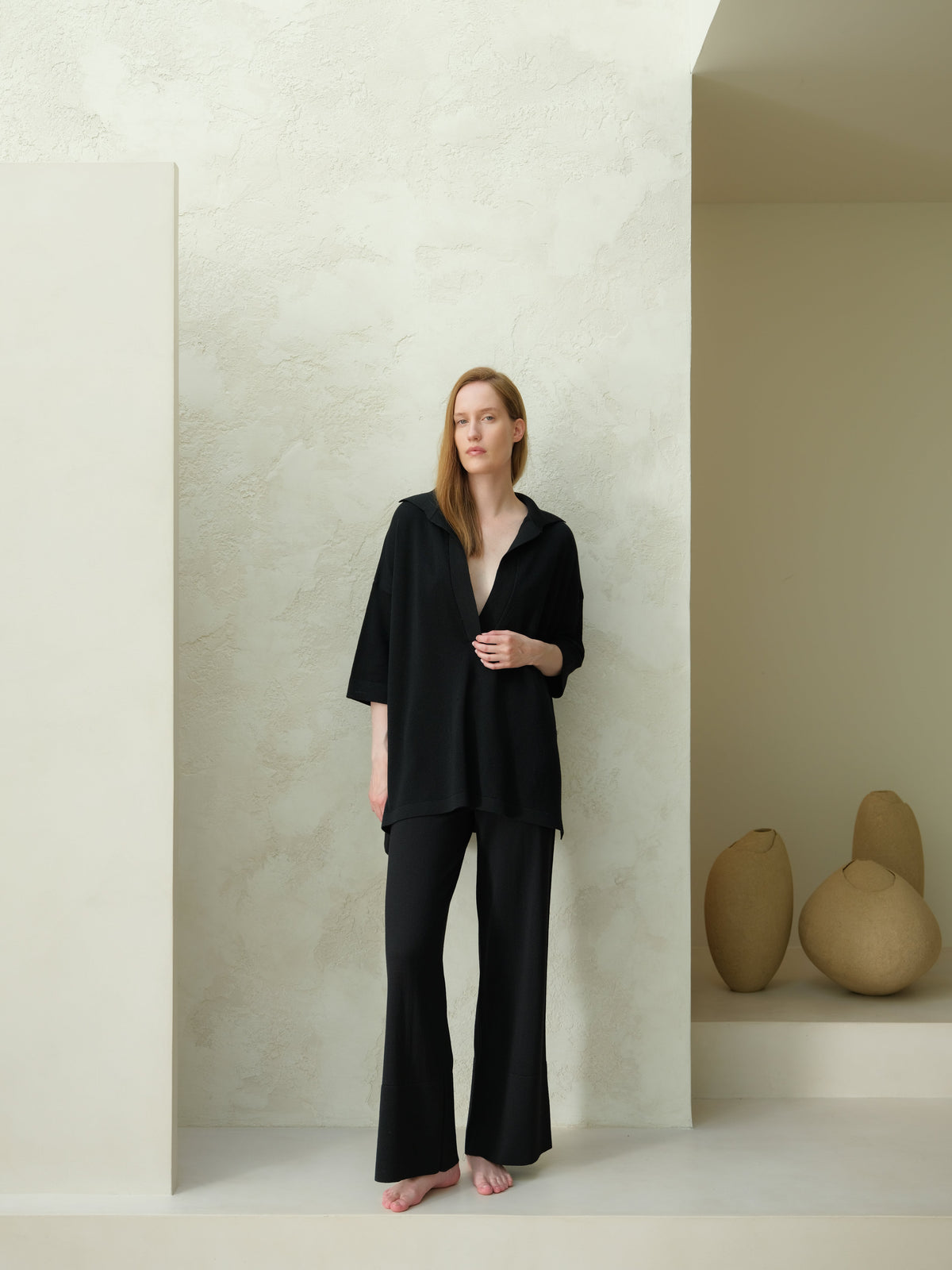 Full-body view of a model in a black Maxi polo de lana merina extrafina paired with pantalones de pierna ancha in a minimalist studio.