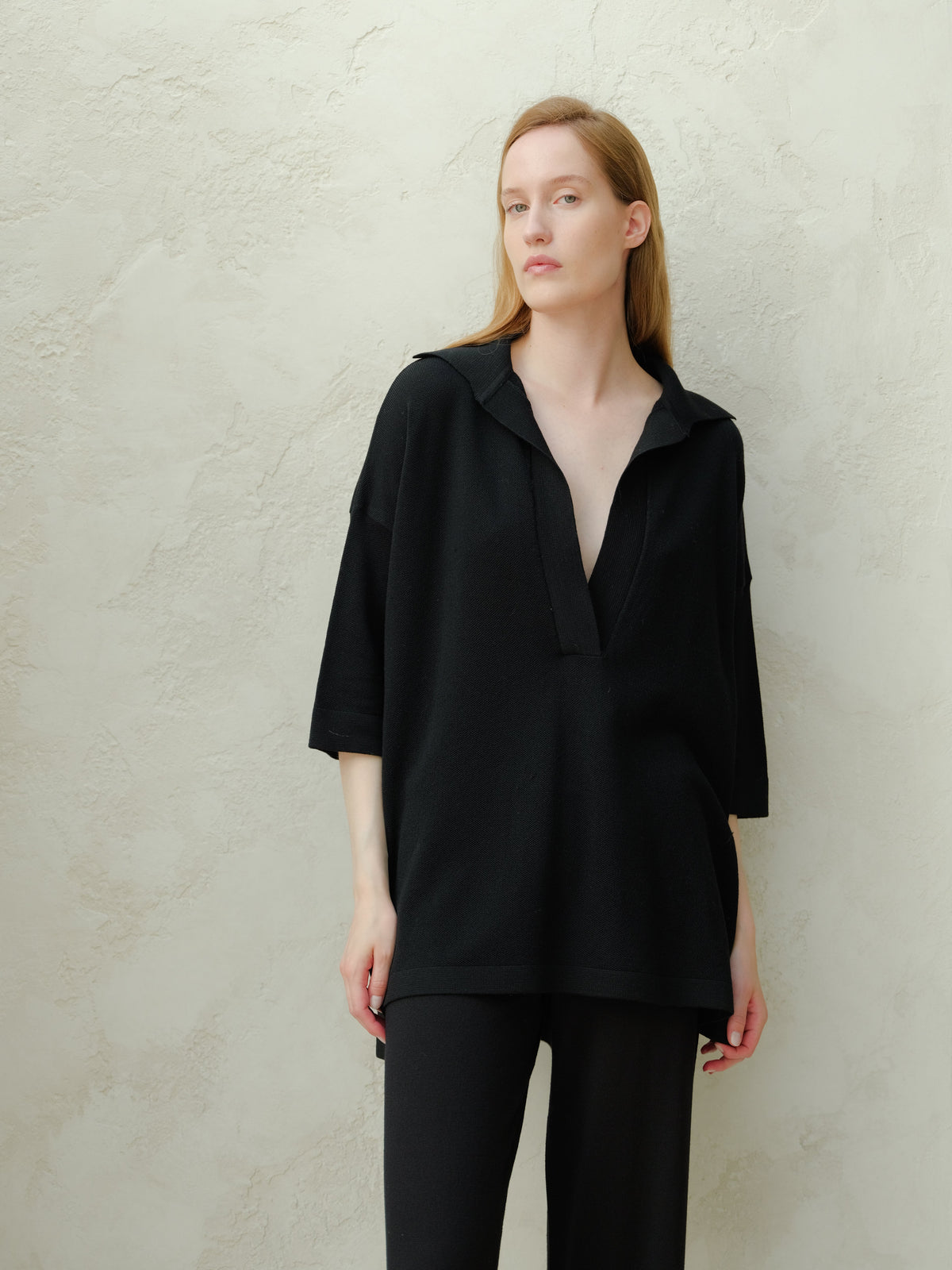 Mujer con black oversized merino wool maxi polo with deep V-neck and relaxed silhouette.