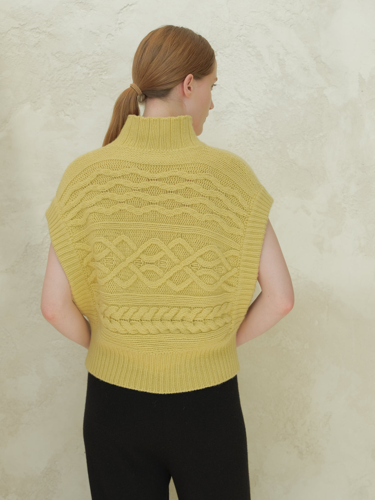 Back view of a pale yellow cable knit maxi tunic with hoher Kragen and intricate patterns.