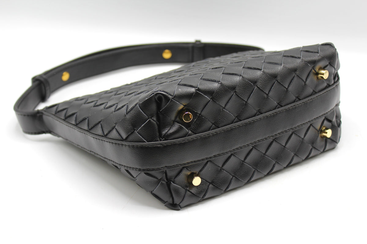 Vue en angle d’une pochette rectangulaire en cuir noir tressé avec clous dorés et bords surpiqués