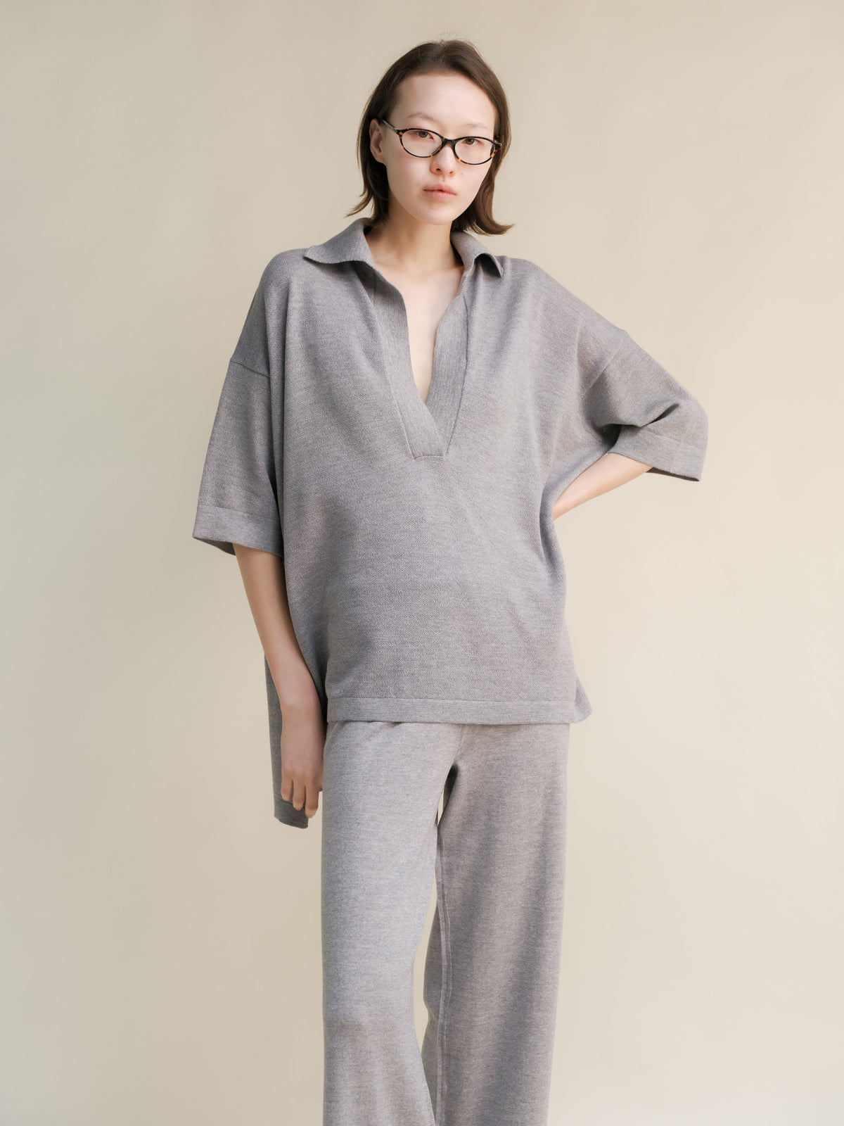Mujer con oversized light gray merino wool maxi polo with deep V-neck and pantalones de pierna ancha a juego.
