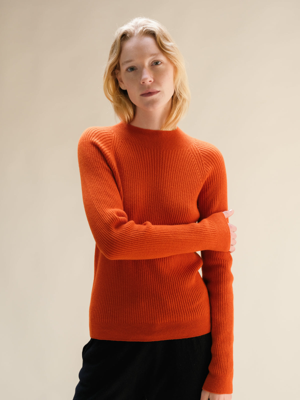 Model draagt a bright orange ribbed cashmere mix mock neck sweater.