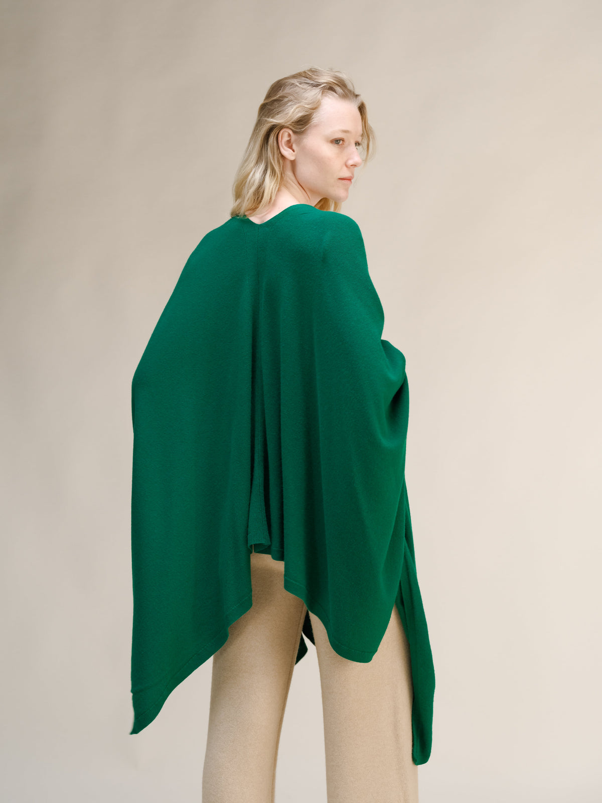 Vista posterior de una modelo con capa maxi verde de mezcla de cachemira sobre los hombros y pantalón beige