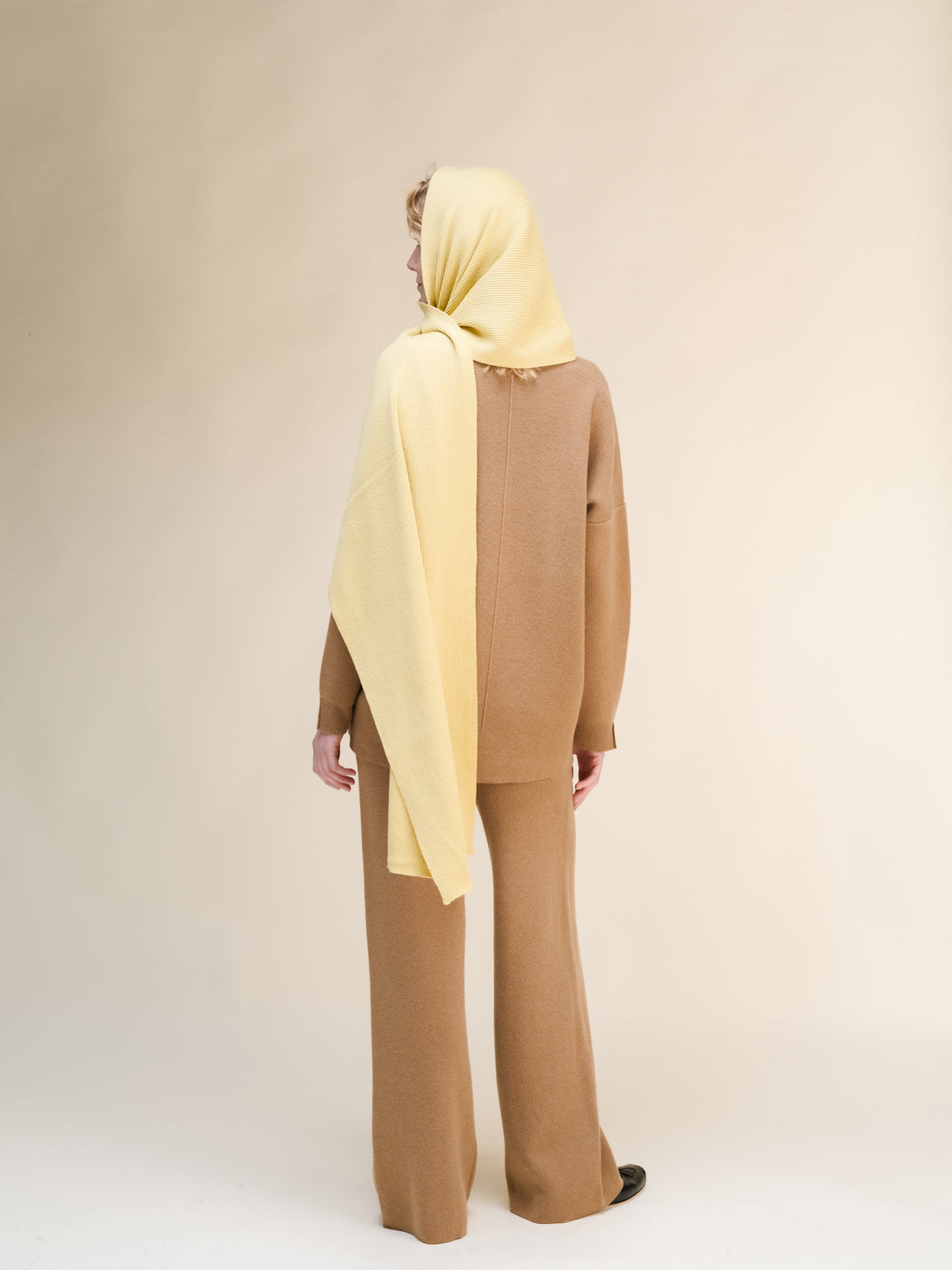 Persona con hijab beige e outfit marrone su sfondo uniforme.