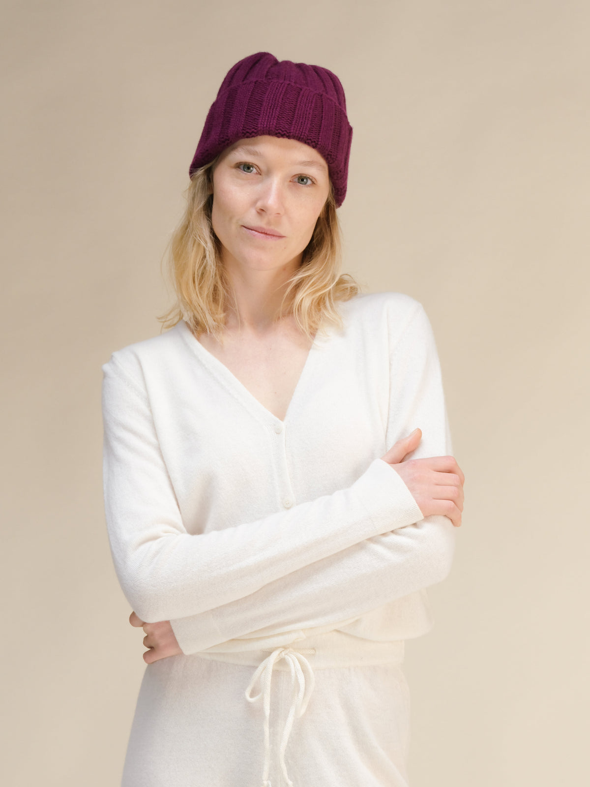Femme en pull blanc avec bonnet bordeaux sur fond beige.