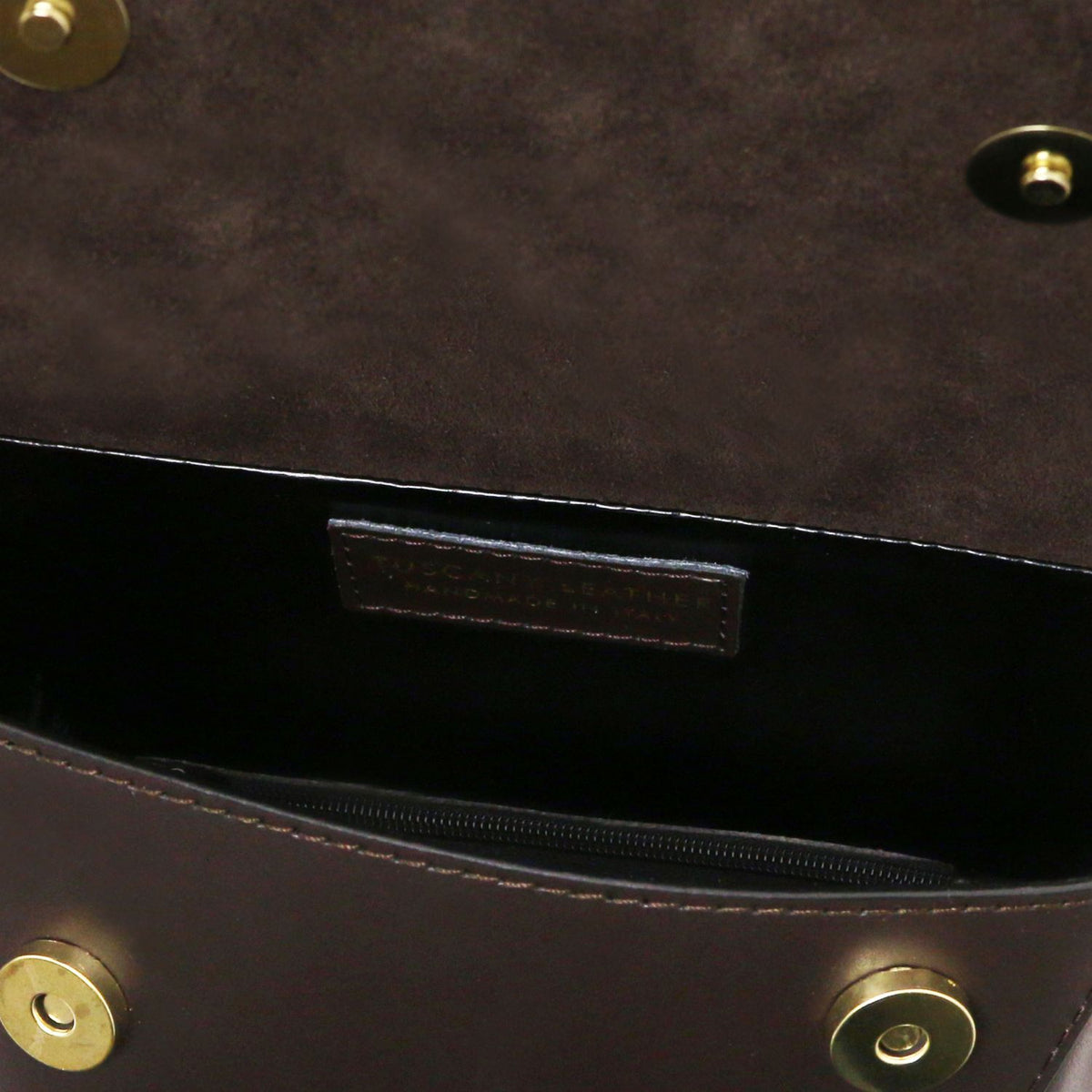Primer plano of a dark brown leather handbag interior mostrando a bolsillo con cremallera, a forro interior negro, and brass-tone hardware.