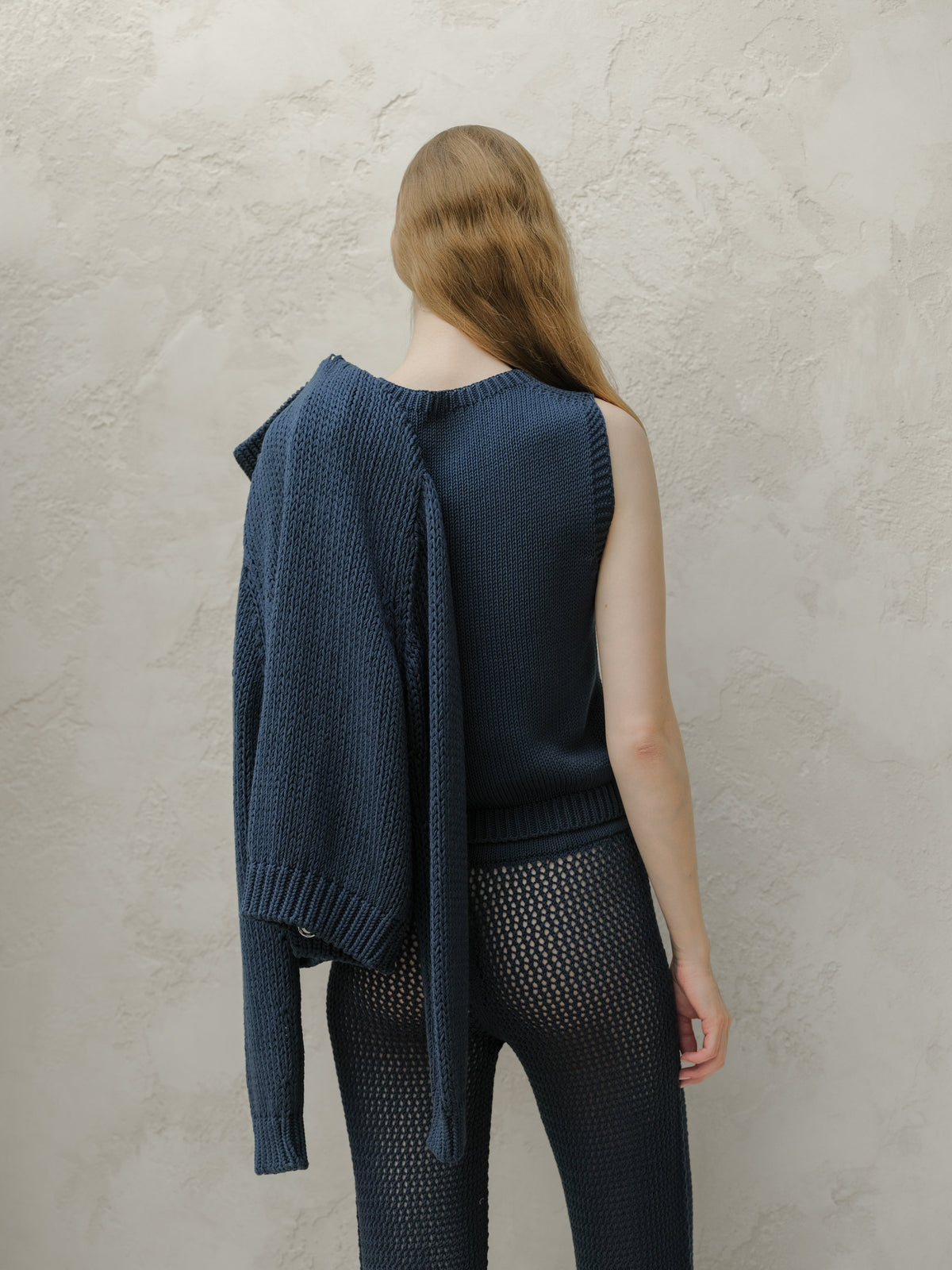 Back view of a modella con a blu navy knit top con a cardigan draped over one shoulder e sheer knit pants