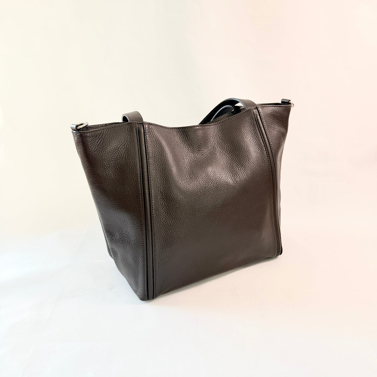 Borsa tote in pelle martellata marrone scuro con manici su sfondo bianco avorio.