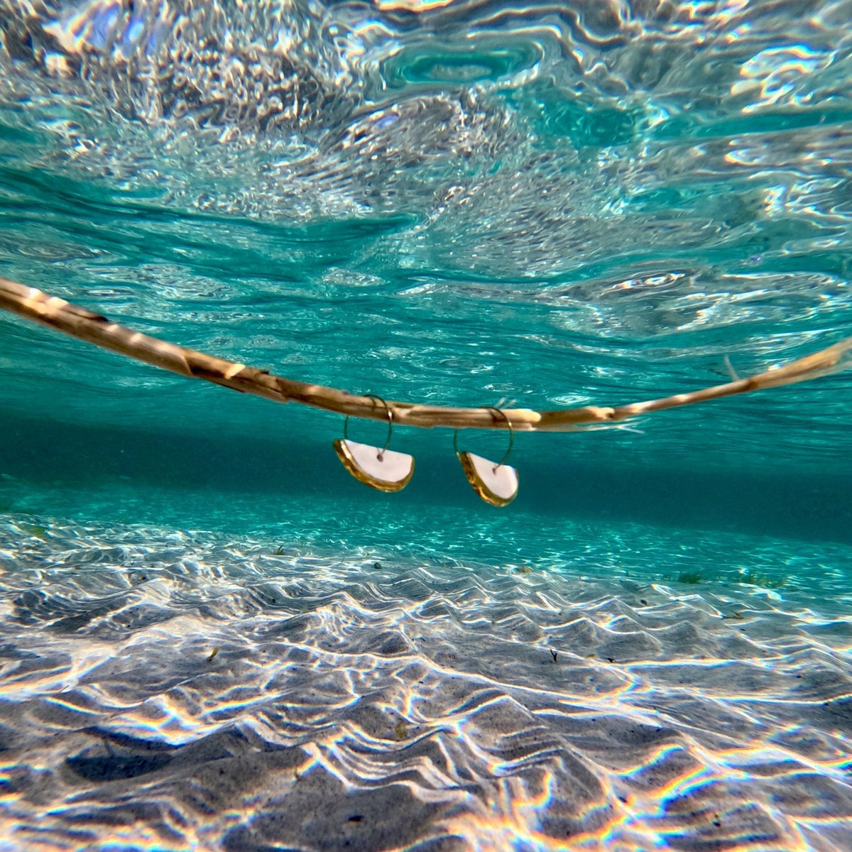 Orecchini in ceramica con bordi dorati nell’acqua azzurra limpida sopra un fondale sabbioso