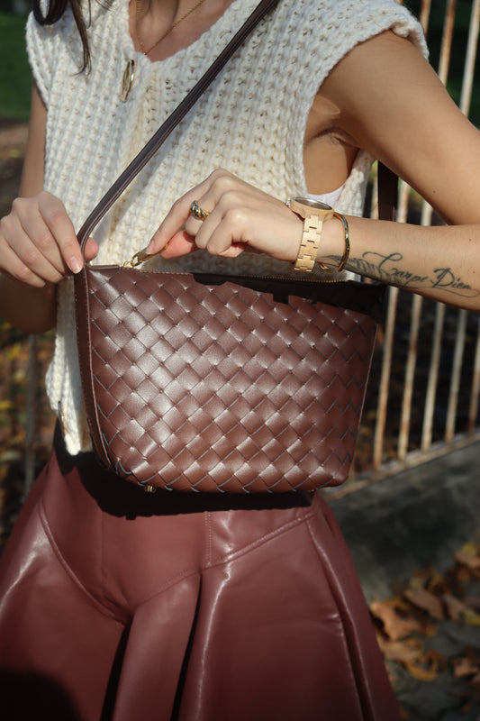 Modelo con bolso pouch rectangular de piel tejida marrón y correa larga sobre un top de punto blanco