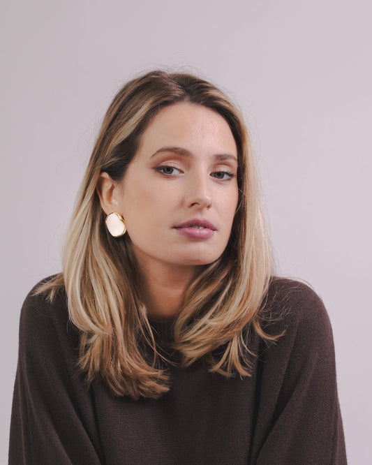 Mulher com white and gold ceramic earrings with a brown sweater against a plain background