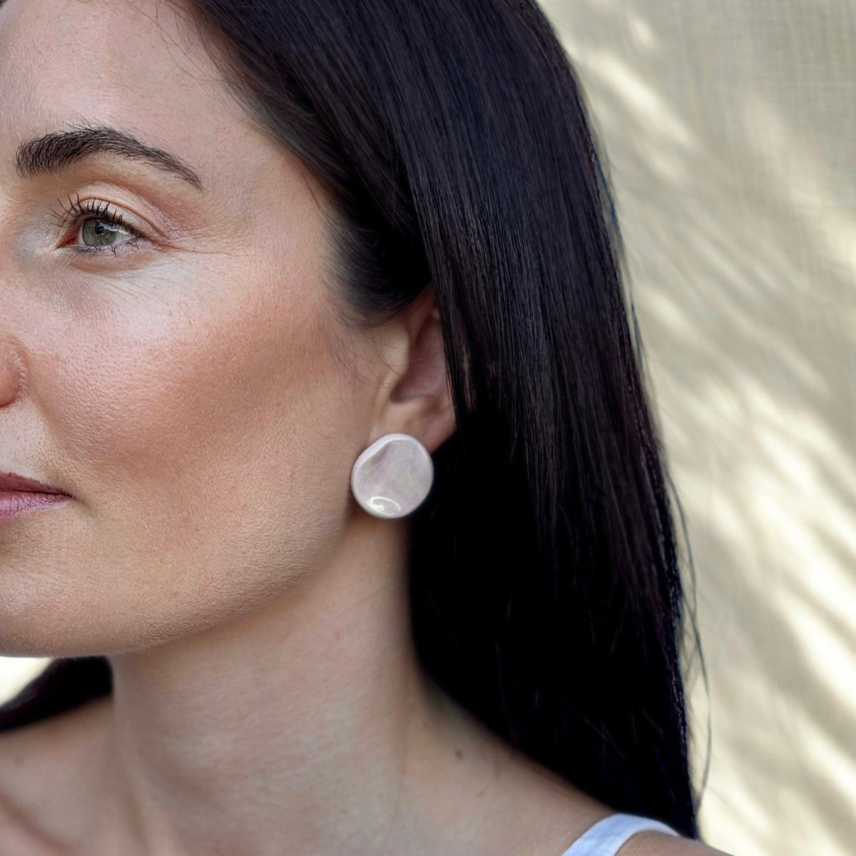 Pearl pink ceramic stud earrings worn on the ear.