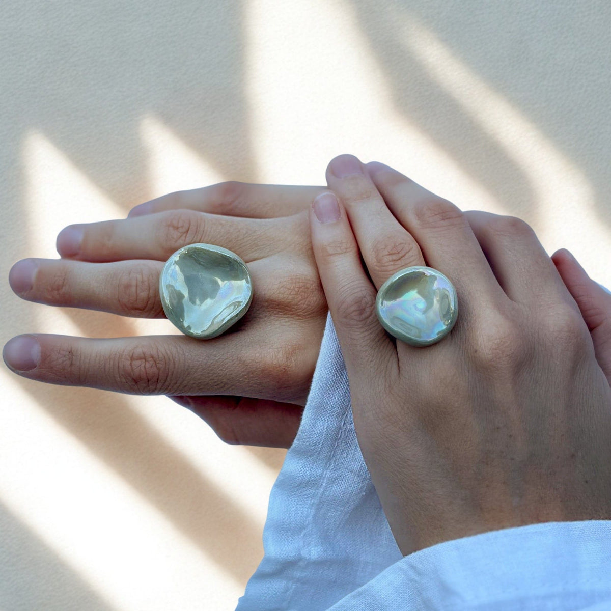 Dos manos con grandes anillos Perla de cerámica verde salvia en dedos contiguos