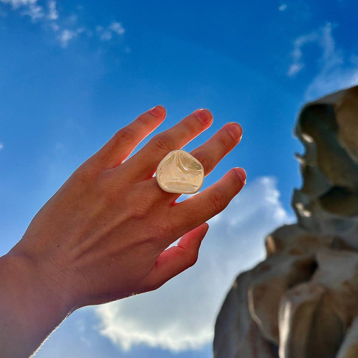Pearl white ceramic ring on a finger with a clear blue sky as backdrop.