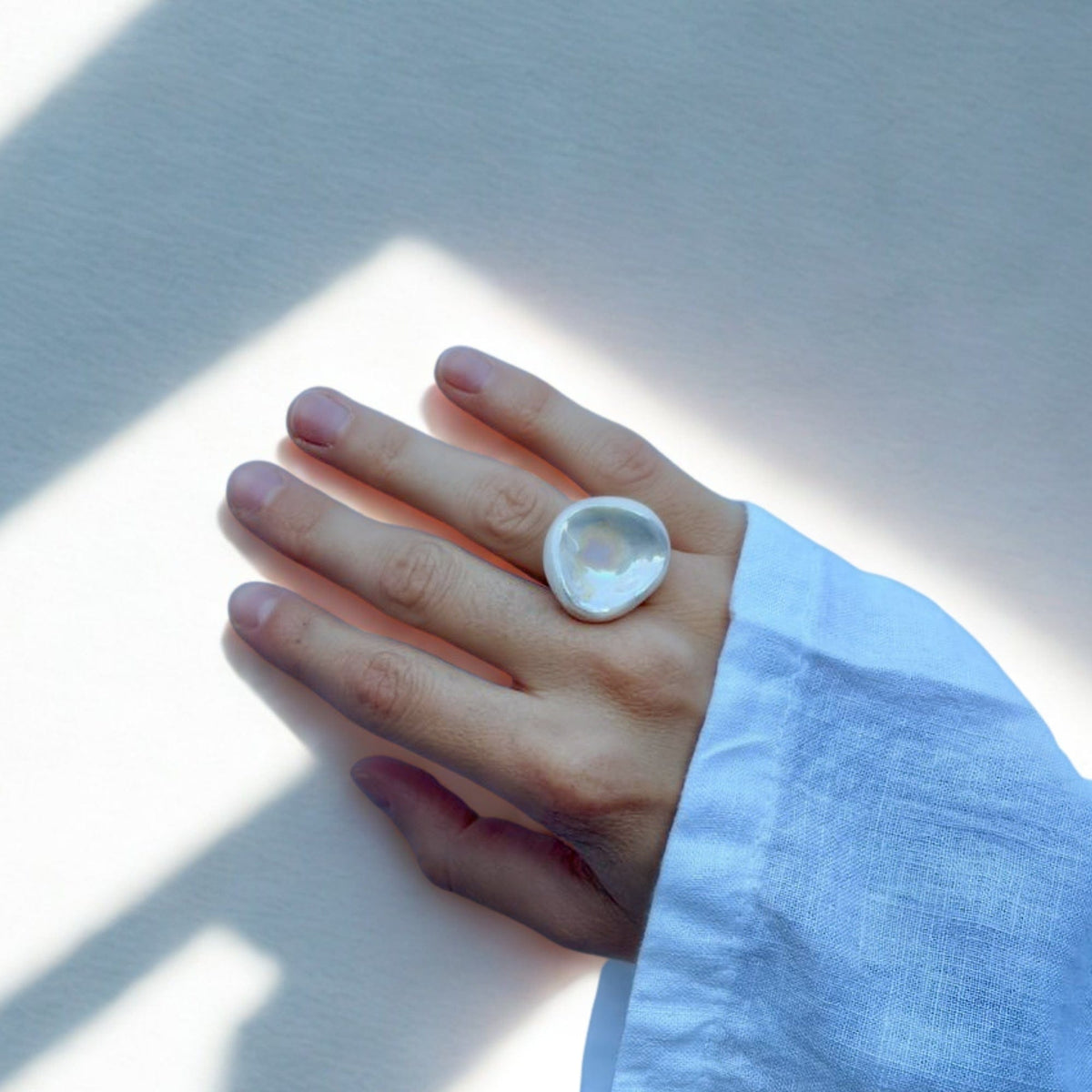 Hand showing a single oversized pearl white ceramic ring on the middle finger.
