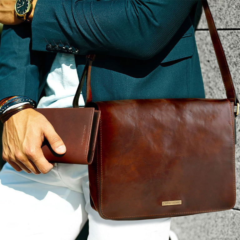 Bolso mensajero bandolera de piel marrón con una pequeña cartera, llevado por una persona con blazer color verde azulado