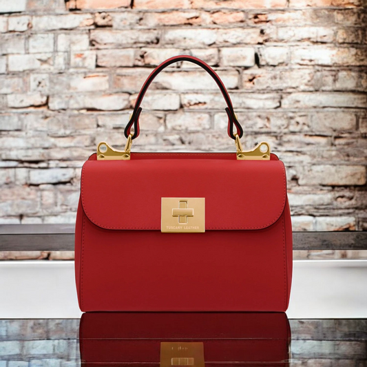 Strukturierte rote Lederhandtasche mit goldfarbenem Verschluss und Henkel vor einer Backsteinwand.