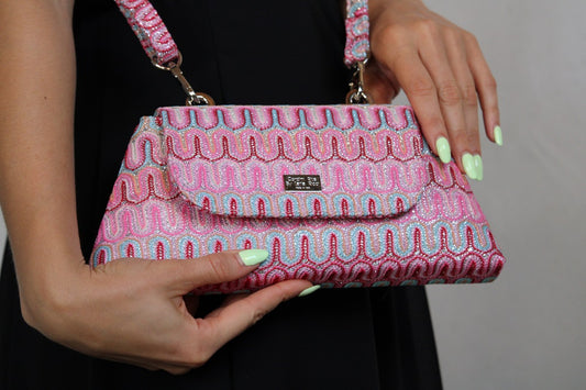 Roze handtas met patroon en golvend ontwerp, vastgehouden door een persoon met mintgroene nagels.