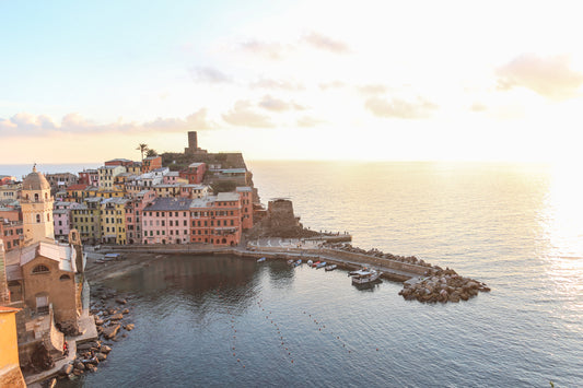Door de zonsondergang verlicht uitzicht op een kleurrijk Italiaans kustdorp met haven en boten.