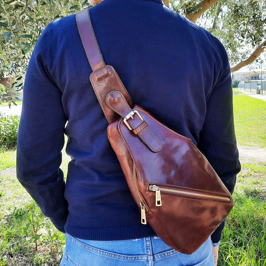 Bruine leren slingbag diagonaal over de borst gedragen door een persoon in een marineblauwe trui