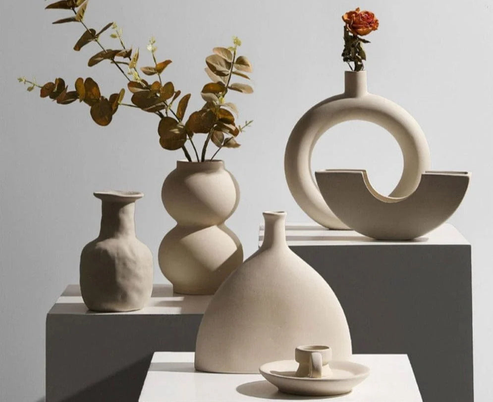 Vasi in ceramica dai toni neutri e ceramiche scultoree disposti su piedistalli in un allestimento minimalista