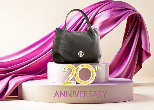 Schwarze Handtasche aus strukturiertem Leder auf einem pastellfarbenen Podest mit fliessendem violettem Stoff für eine Ausstellung zum 20-jährigen Jubiläum.