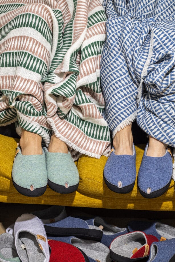 Two people wearing blue and green striped slippers sit with striped blankets on a yellow sofa