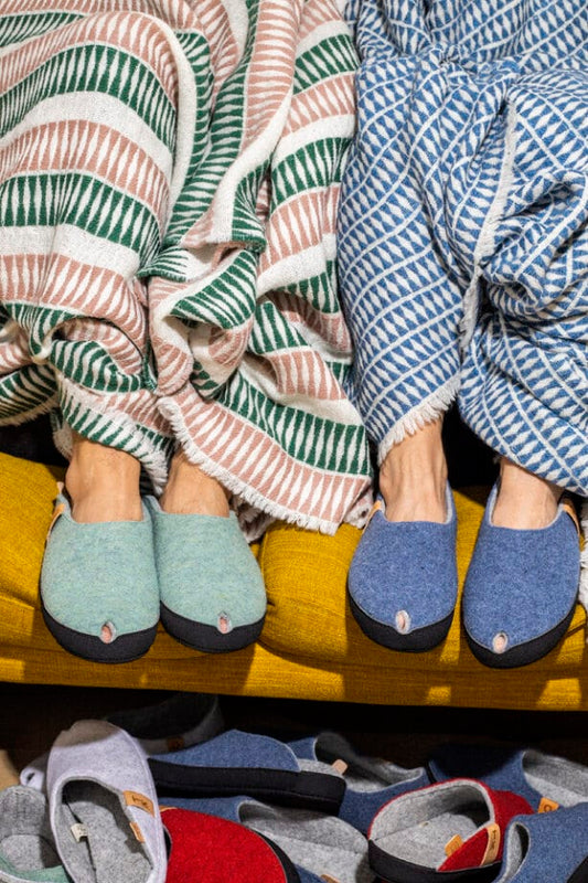 Two people wearing blue and green striped slippers sit with striped blankets on a yellow sofa