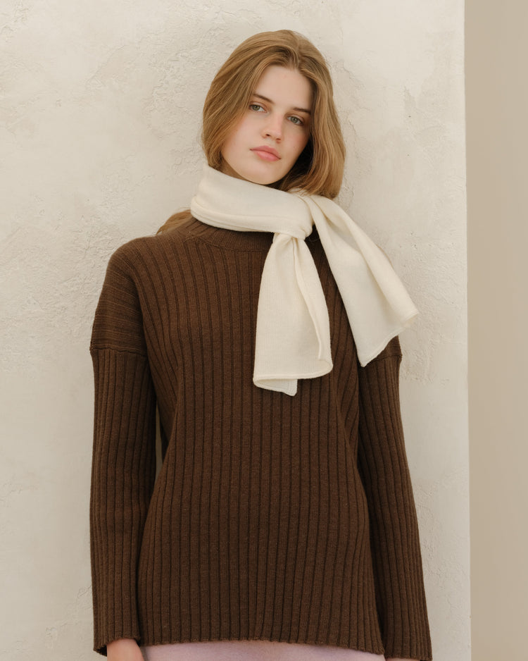 Modella con maglione marrone in maglia a coste e sciarpa color crema avvolta intorno al collo.