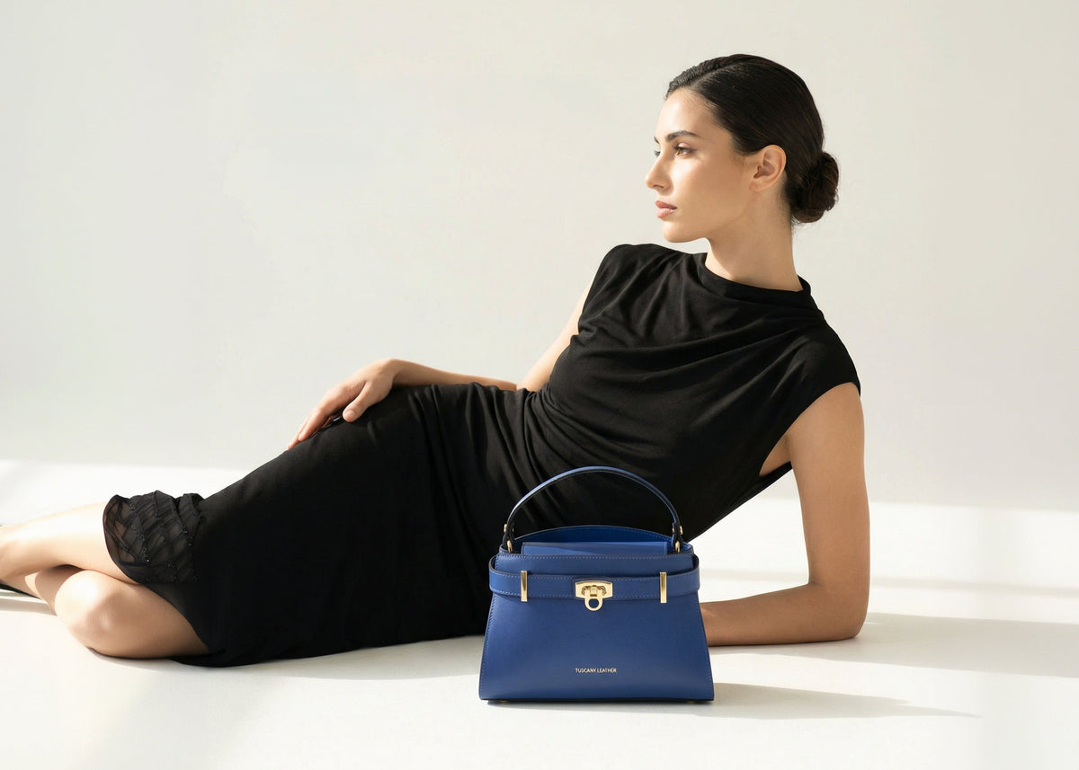 Blue handbag with gold hardware resting beside a reclining woman in a black dress.