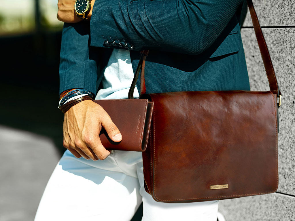Hand hält eine braune Lederbörse neben einer passenden braunen Leder-Messenger-Tasche.