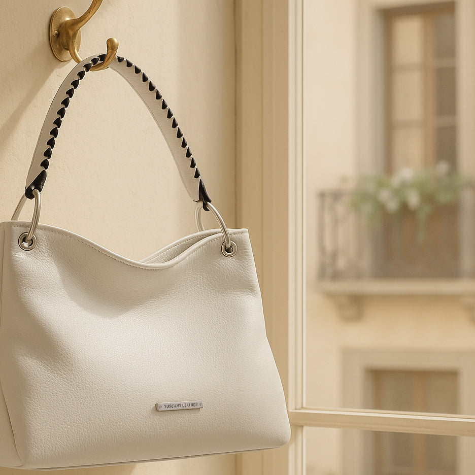 White handcrafted leather handbag with braided handle hanging on a wall hook by a sunlit window in an Italian apartment.