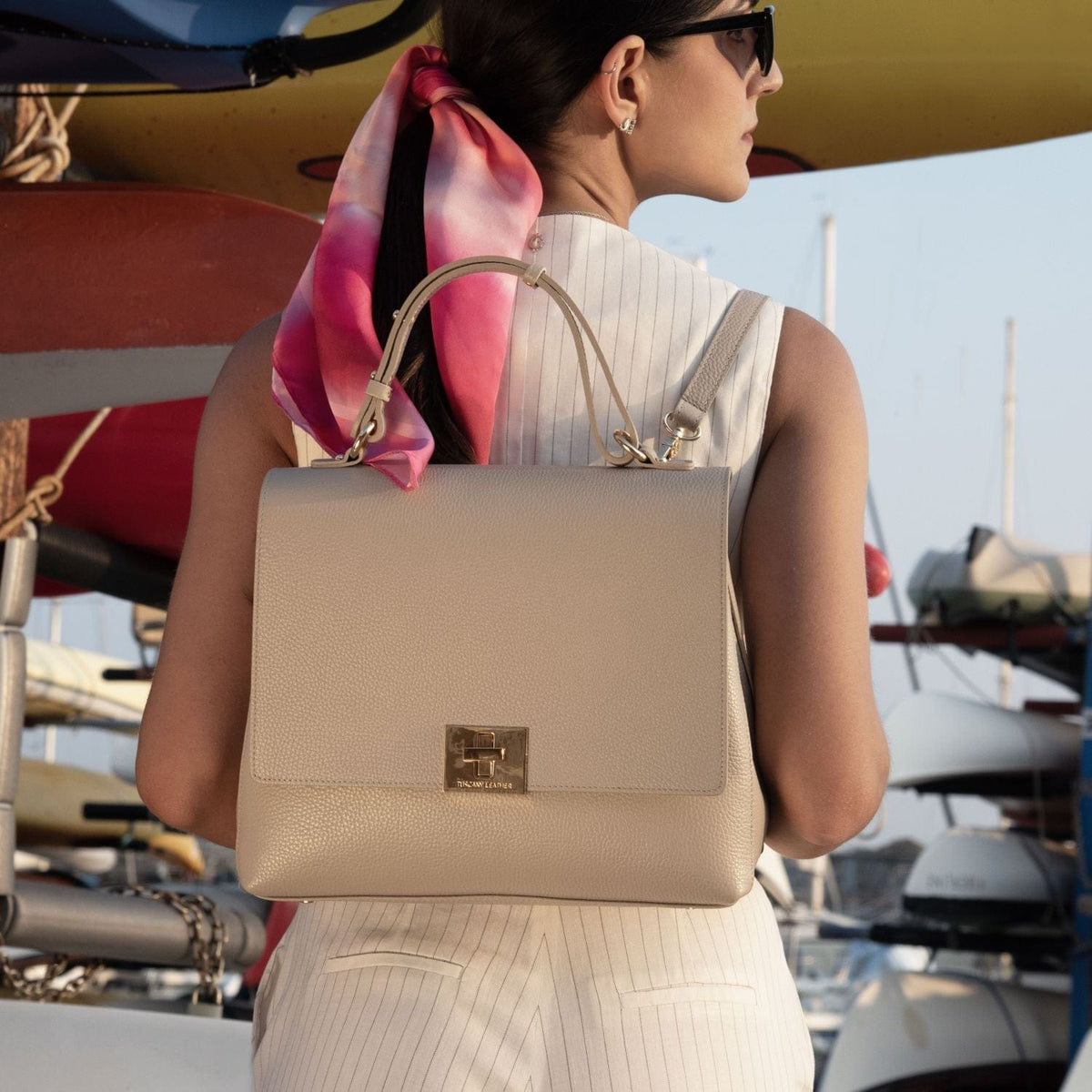 Beige pebbled leather handbag with gold hardware carried by a woman near a marina.