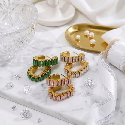 Oro hoop earrings con verde e rosa gemstones on a marble surface.