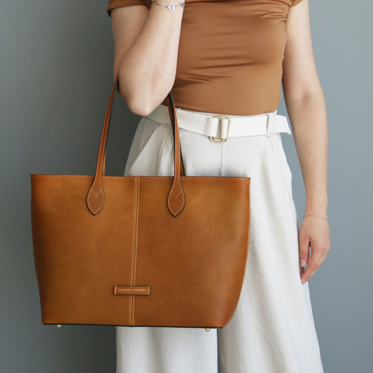 Person holding a brown leather tote bag against a gray background