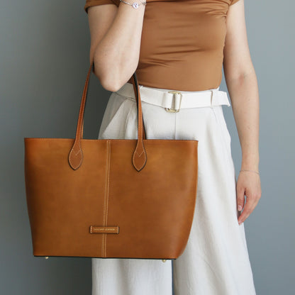 Person holding a brown leather tote bag against a gray background