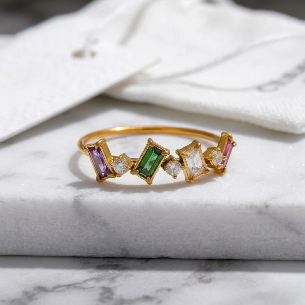 Gold ring with colorful gemstones on a marble surface