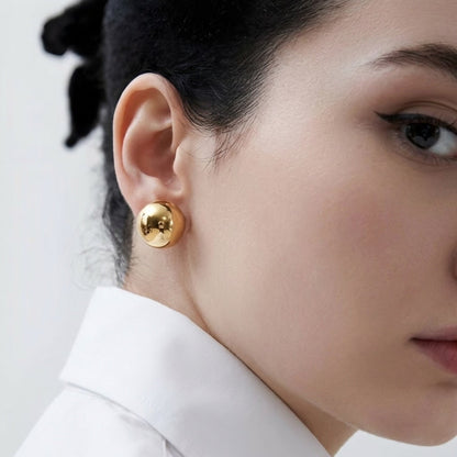 Primer plano of a person wearing gold earrings with a neutral background