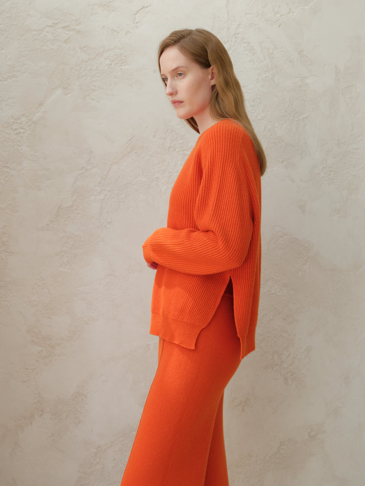 Profile view of a model in a bright orange ribbed knit sweater with pantalones a juego.