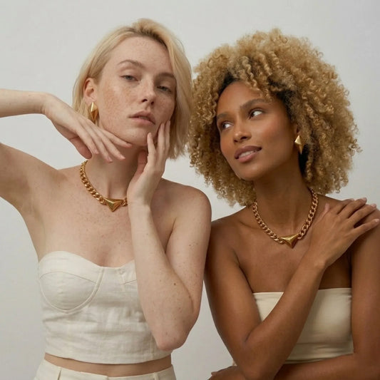 Two women wearing gold necklaces against a plain background