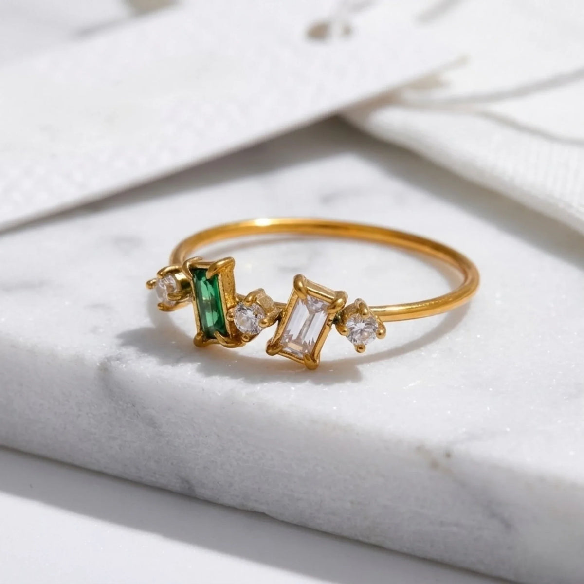 Gold ring with emerald and diamond accents on a marble surface