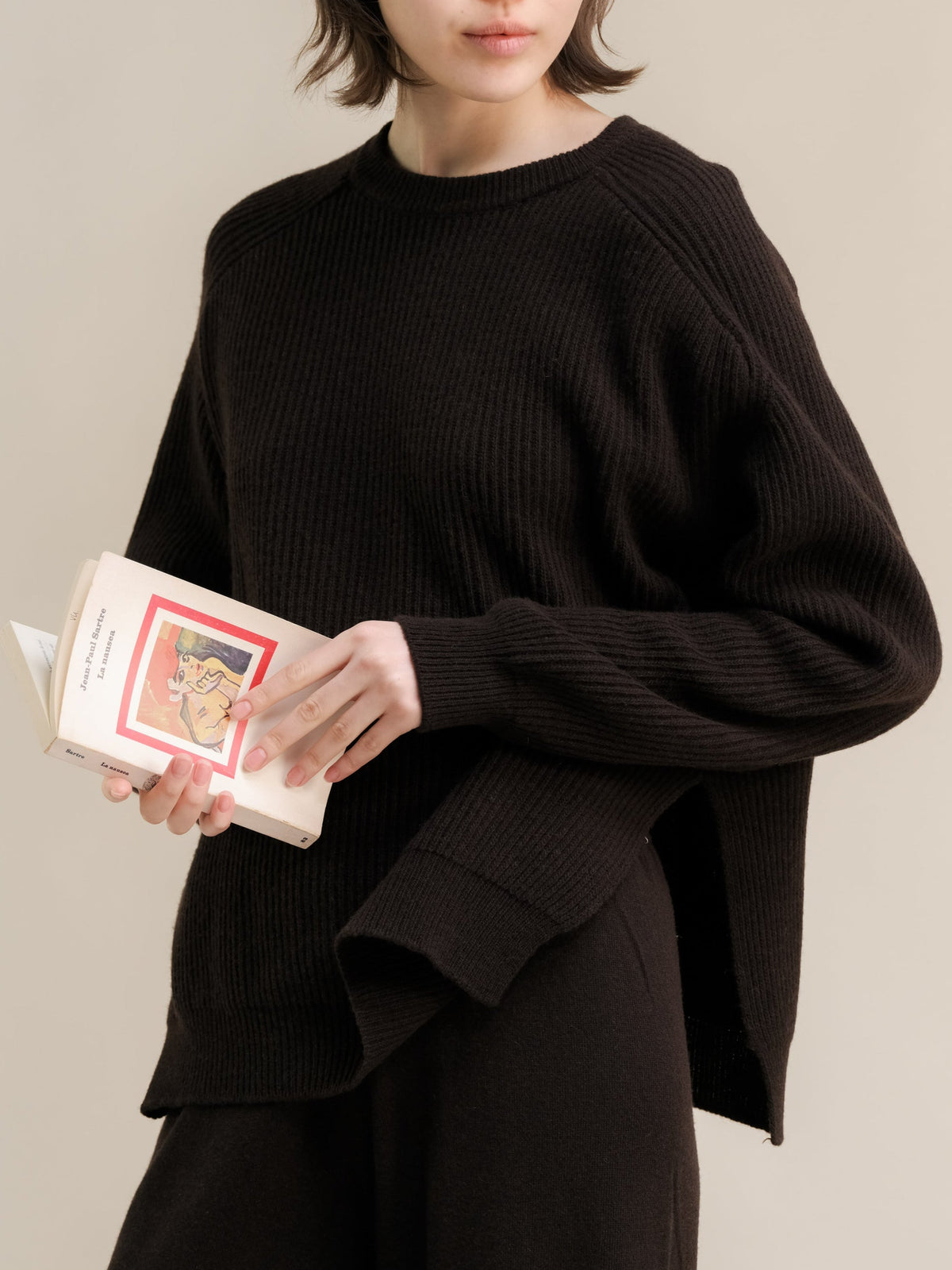 Modelo con black ribbed cashmere mix jersey de cuello redondo with lateral side slits while holding a book