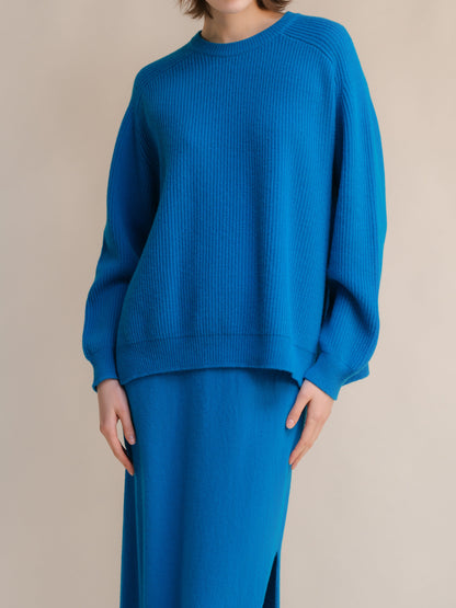 Bright blue ribbed jersey de cuello redondo with side slits worn by a model against a neutral background