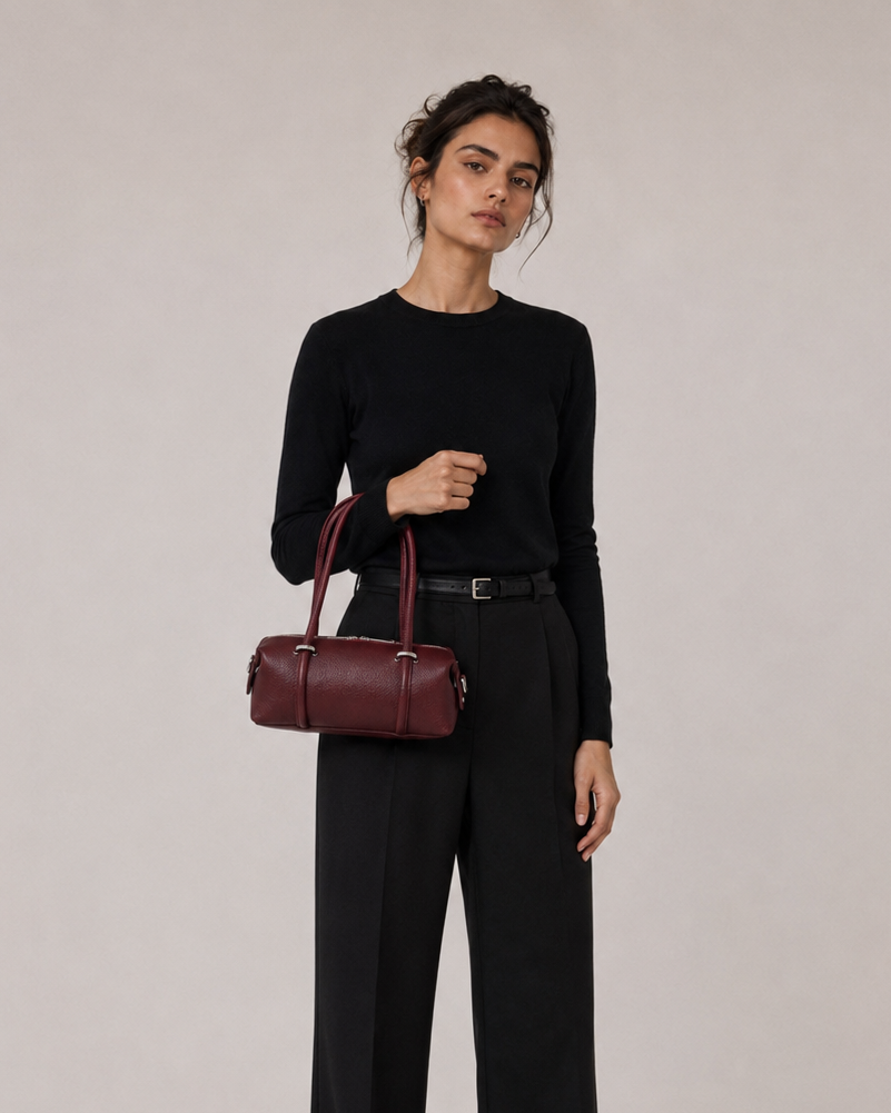 Woman holding a burgundy handbag against a plain background