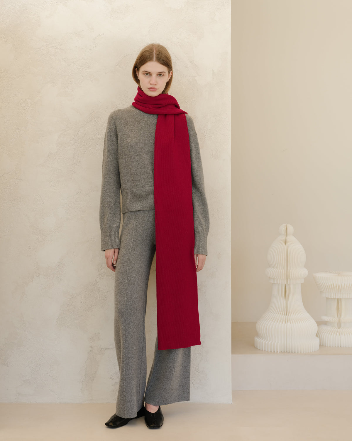 Person wearing a gray outfit with a long red scarf against a neutral background
