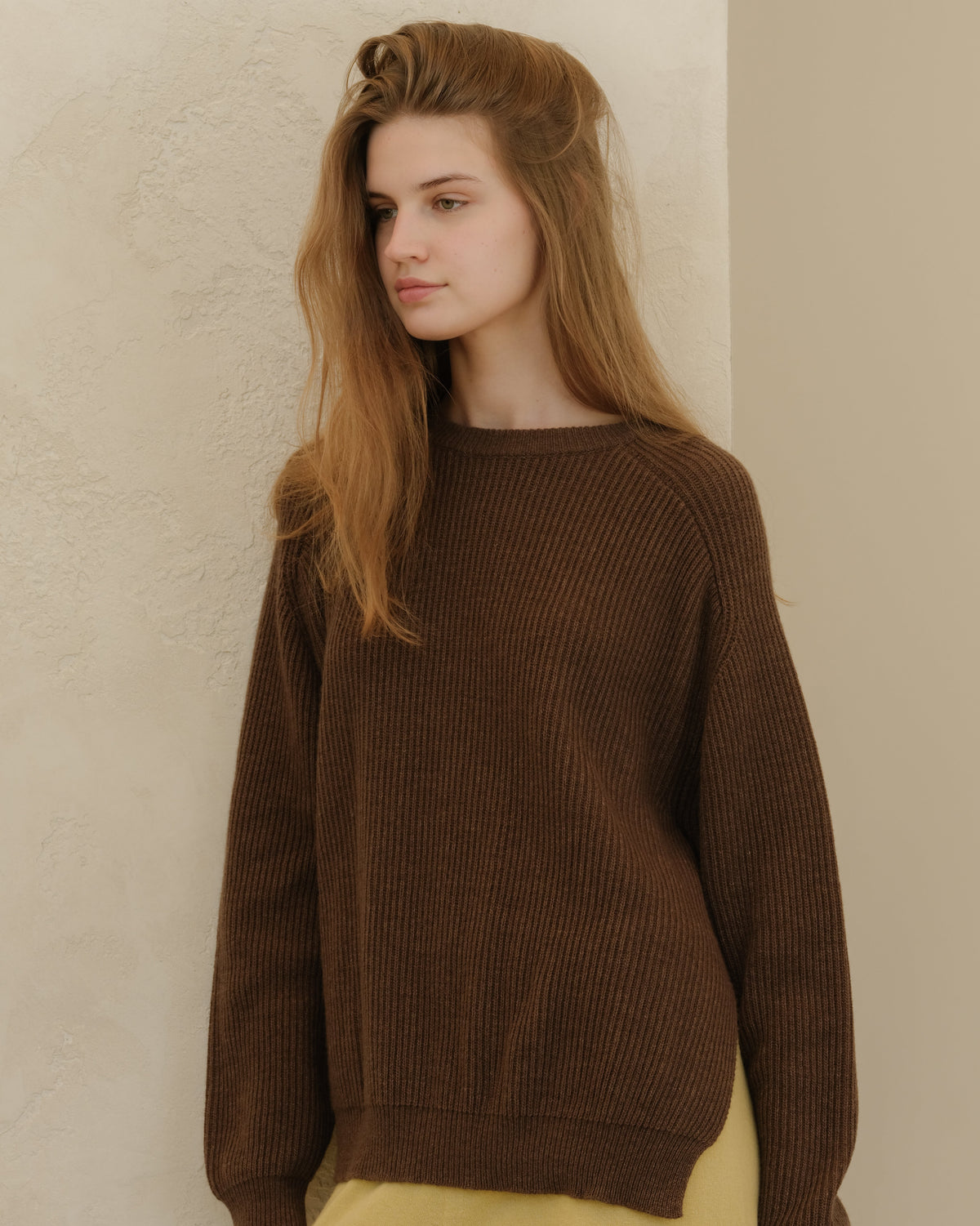 Close-up of a model in a brown ribbed knit sweater with a corte relajado and pale yellow pants.