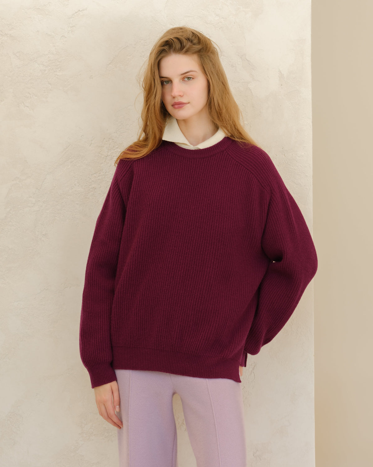 Modelo con burgundy Cashmere Mix Crewneck Ribbed Sweater with Lateral Slits and a white collar peeking out against a light textured wall.