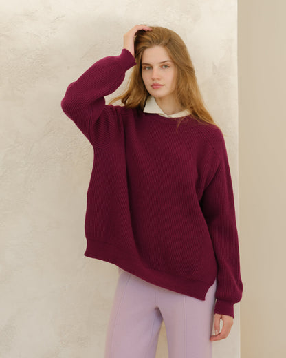 Modelo con burgundy cashmere mix crewneck ribbed sweater with side slits against a textured beige wall.